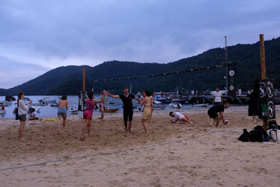 Un viaje en grupo de WeRoad jugando voleibol de playa en una orilla arenosa con barcos y montañas de fondo.