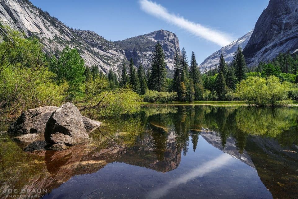 Un lago placido riflette montagne di granito, alberi verdeggianti e un cielo azzurro limpido.