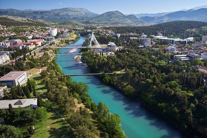 Una vista aerea di una città attraversata da un fiume turchese, con diversi ponti e le montagne sullo sfondo.