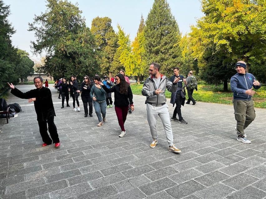 Un viaggio di gruppo WeRoad pratica Tai Chi con un istruttore su un viale pavimentato in un parco.