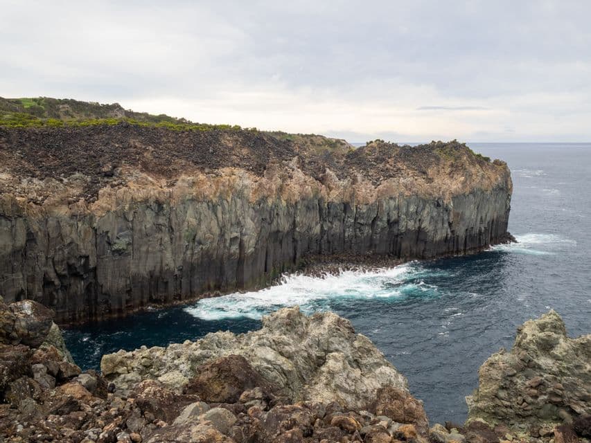 De hautes falaises de basalte colonnaire rencontrent l'océan, avec des vagues blanches s'écrasant à leur base par une journée nuageuse.