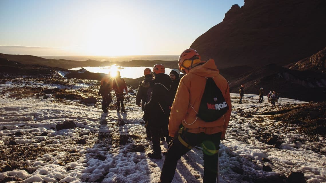 Un viaje en grupo de WeRoad recorre un paisaje nevado y rocoso, caminando hacia el sol bajo en el horizonte.