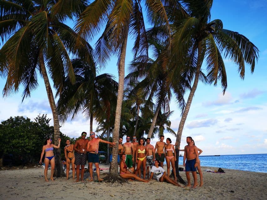 Un viaje en grupo de WeRoad en traje de baño posando para una foto en una playa de arena bajo altas palmeras.