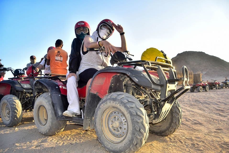 Viaje en grupo WeRoad en quads rojos por el desierto, con dos personas en primer plano posando para la cámara antes de la aventura.