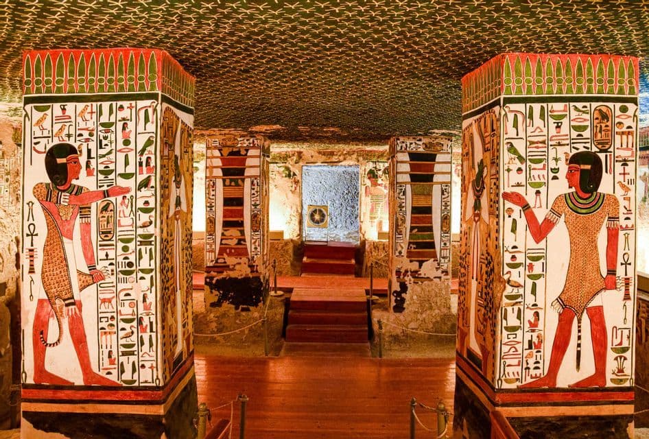 El interior de una tumba egipcia antigua, con grandes pilares cubiertos de jeroglíficos coloridos y figuras pintadas.