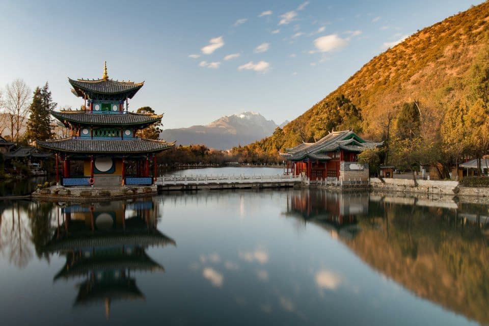 Due tradizionali pagode asiatiche si ergono su un lago calmo, con le loro riflessioni nitide nell'acqua, e una collina boscosa e montagne innevate sullo sfondo.