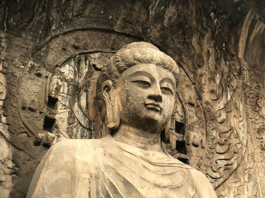 Primo piano di una grande statua di Buddha scolpita nella pietra all'interno di una grotta con intricati motivi sulle pareti.