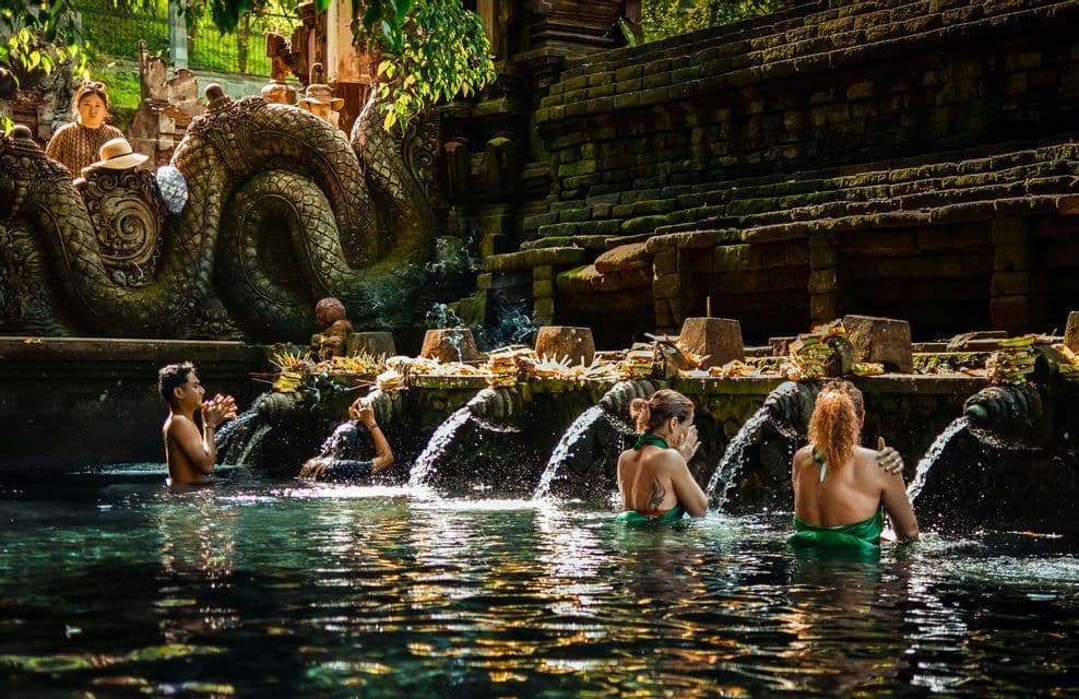 Un viaje en grupo de WeRoad realiza un ritual de purificación en un manantial sagrado, bañándose bajo chorros de agua de piedra.