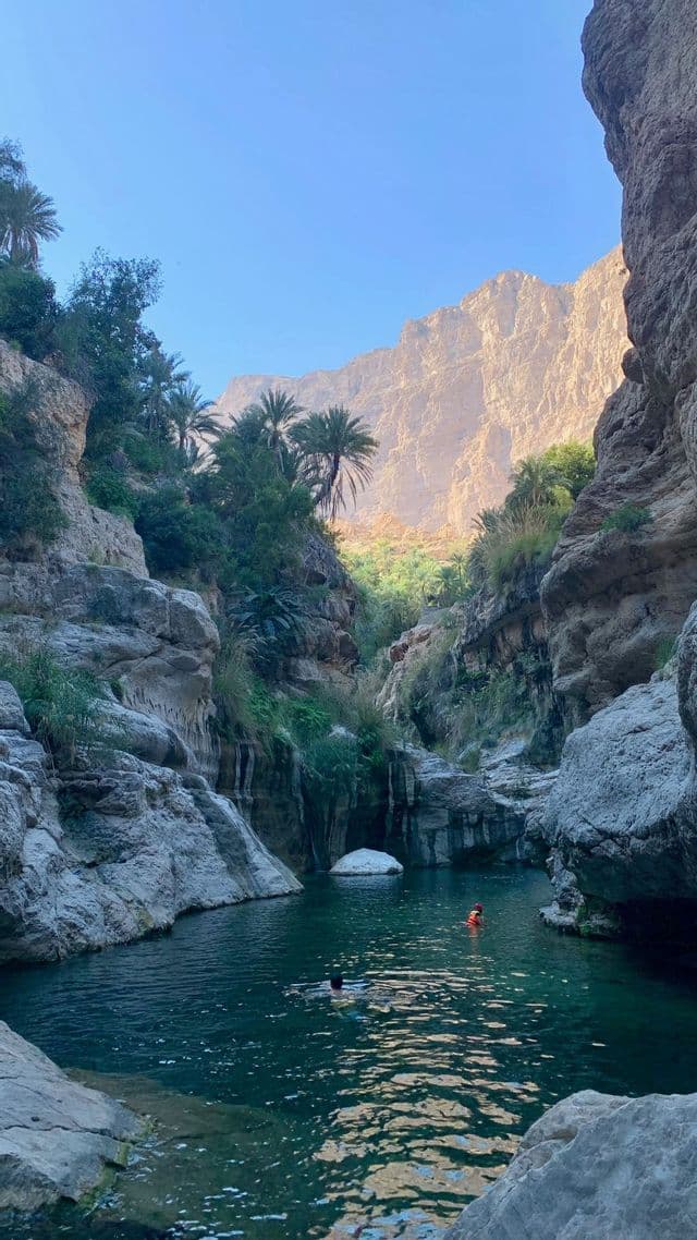 Dos personas en un viaje en grupo de WeRoad nadando en una piscina natural al fondo de un cañón rocoso.