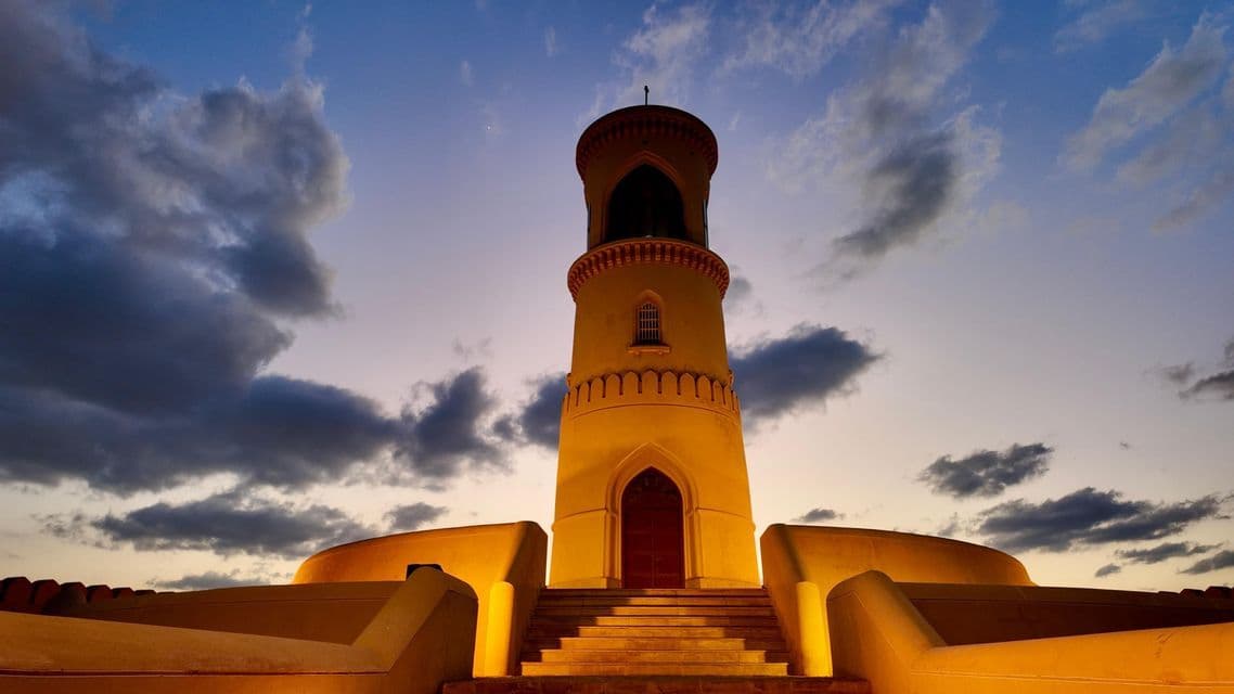 Una toma en contrapicada de una torre amarilla alta iluminada desde abajo contra un cielo nublado al atardecer.