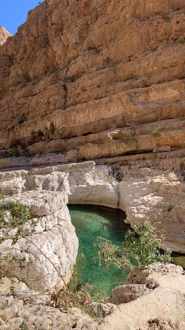 Una persona nada en una piscina de agua turquesa cristalina en el fondo de un cañón rocoso y empinado.