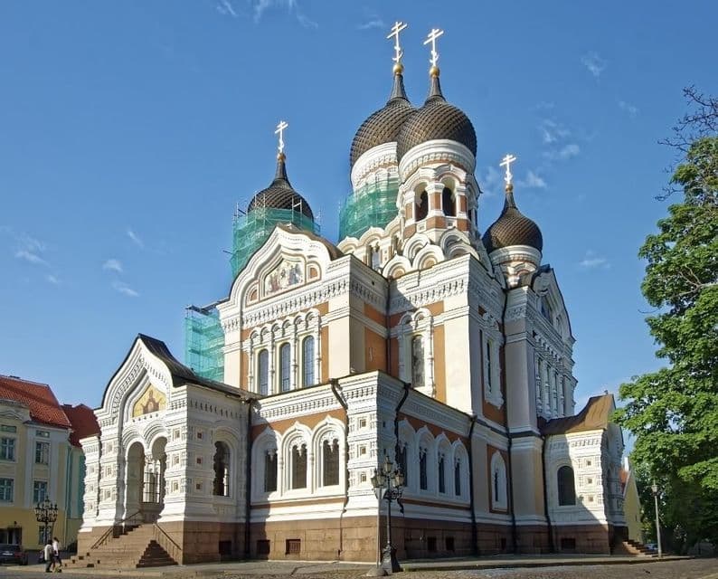 Eine reich verzierte orthodoxe Kathedrale mit dunklen Zwiebeltürmen und goldenen Kreuzen, teilweise von einem Baugerüst verdeckt, unter blauem Himmel.
