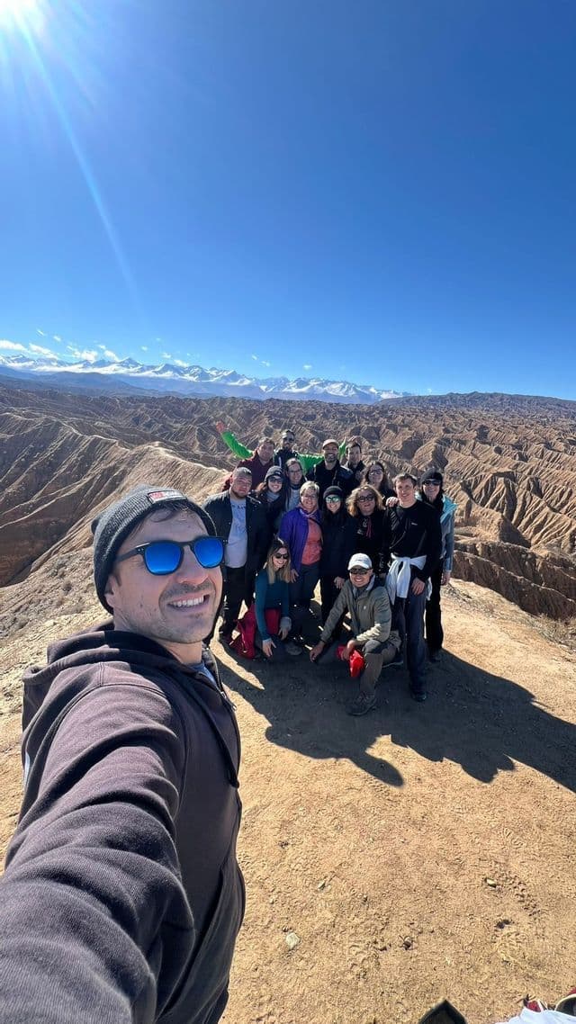 Un gruppo WeRoad scatta un selfie su un crinale soleggiato, con un paesaggio di canyon e montagne innevate alle spalle.