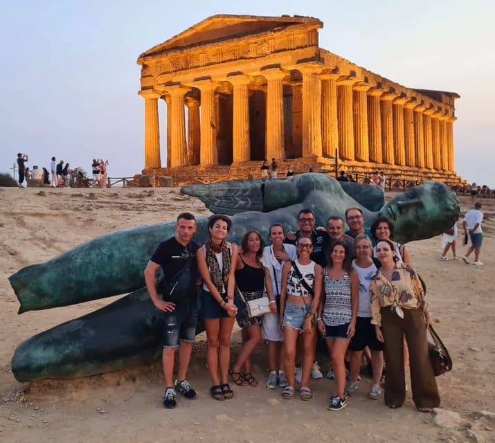 Un viaje en grupo de WeRoad posa junto a una gran estatua reclinada frente a un antiguo templo iluminado por una luz dorada.