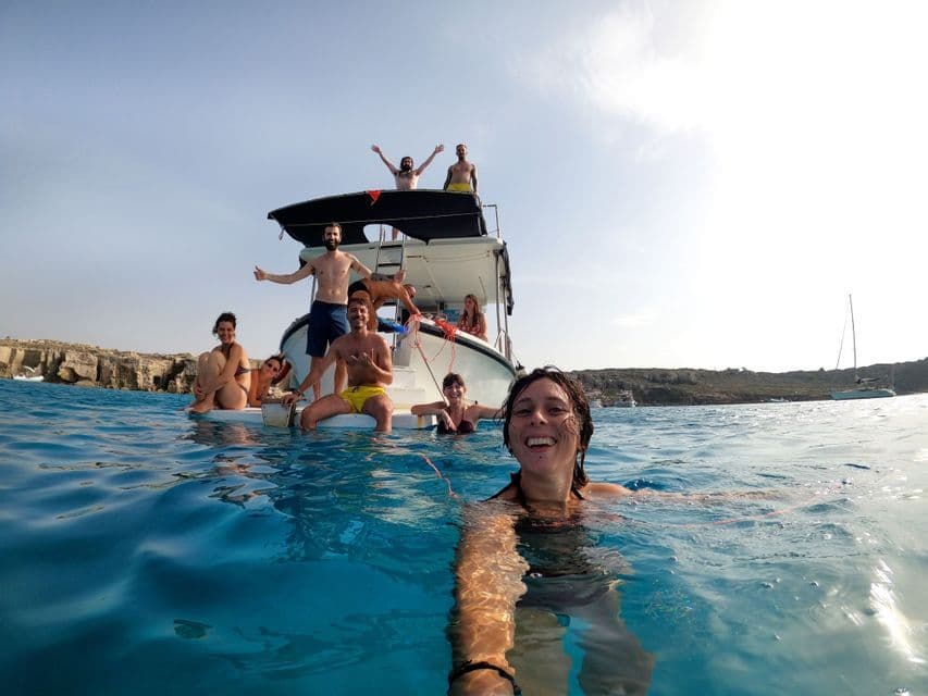Una mujer se toma una selfie mientras nada en el mar, con sus amigos del viaje en grupo de WeRoad en un barco detrás de ella en un día soleado.