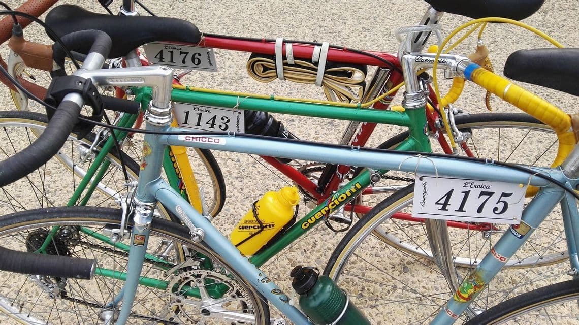 Primo piano di diverse biciclette da corsa vintage colorate con i numeri di gara de L'Eroica attaccati ai telai.