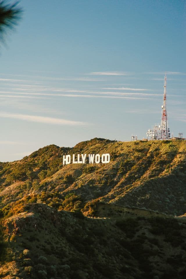El letrero de Hollywood se asienta sobre una colina verde y soleada junto a una gran torre de radio bajo un cielo azul.