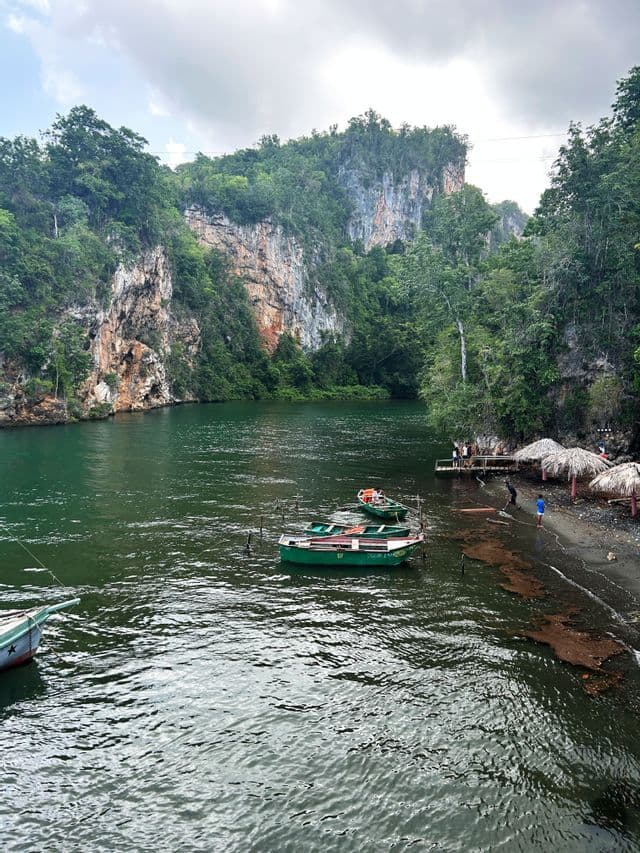 Un viaje en grupo de WeRoad en un muelle de madera junto a un río con barcos verdes amarrados en el agua y un acantilado exuberante al fondo.