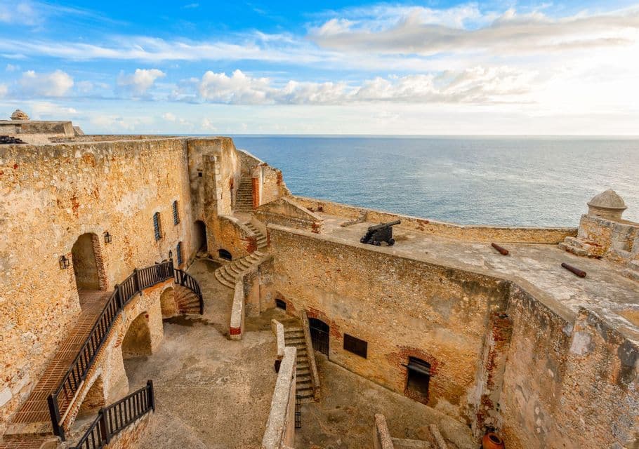Una antigua fortaleza de piedra con cañones en sus murallas, con vistas al océano bajo un cielo azul parcialmente nublado.