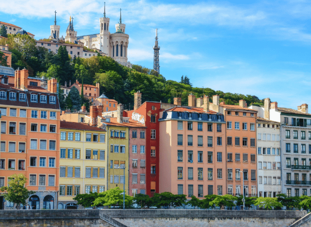 Una fila di edifici colorati si trova sotto una collina verde con una grande basilica in cima, sotto un cielo azzurro e limpido.
