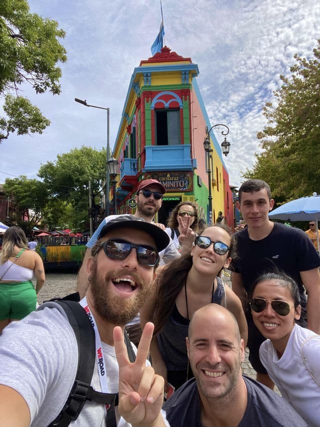 Eine WeRoad-Gruppe lacht und macht ein Selfie auf einer Stadtstraße vor einem mehrfarbigen Gebäude.