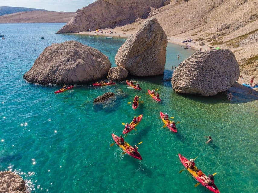 Una vista aerea di un viaggio di gruppo WeRoad in kayak in acqua turchese intorno a grandi rocce vicino a una cala sabbiosa