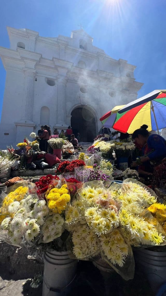 Mercato di fiori all'aperto con bouquet colorati sui gradini di una grande chiesa coloniale bianca sotto il sole.