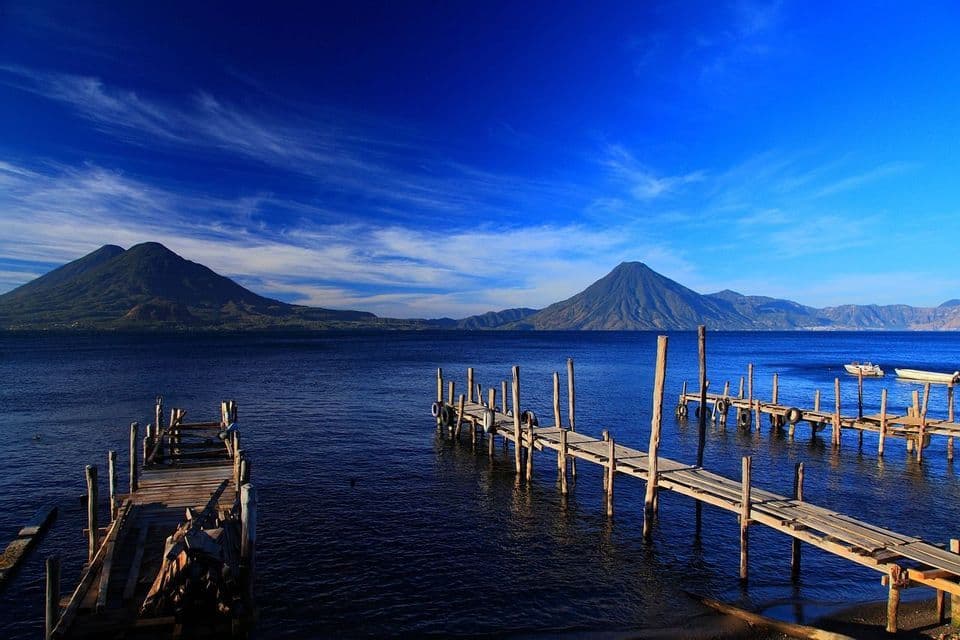 Pontili di legno che si estendono in un lago blu profondo con montagne vulcaniche all'orizzonte sotto un cielo sereno.