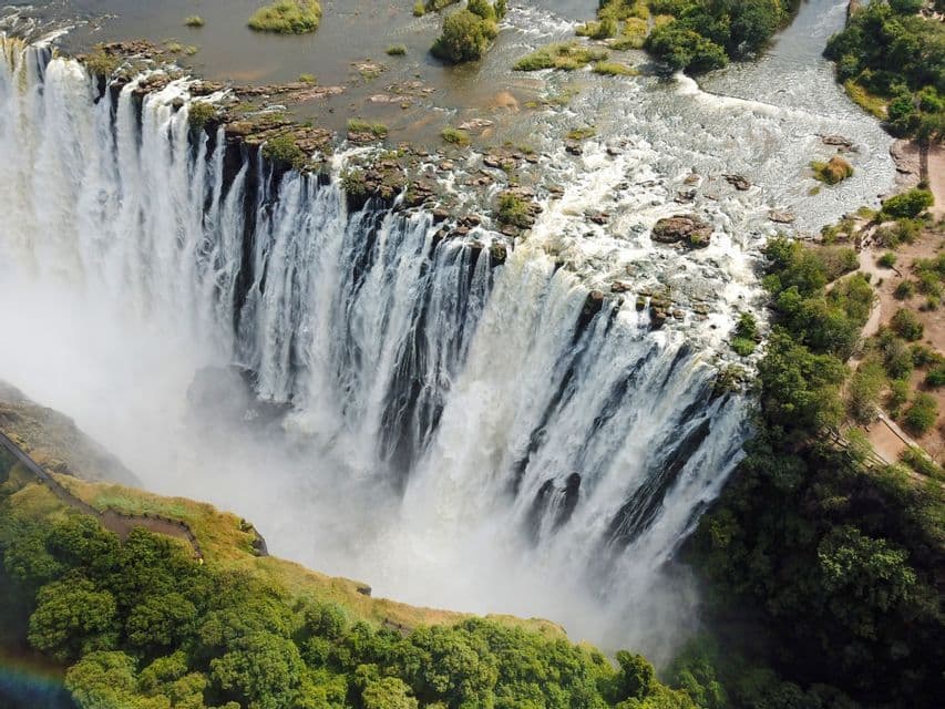 Una vista aerea di una cascata imponente che si getta da un'ampia scogliera rocciosa in una gola nebbiosa circondata da alberi verdeggianti.