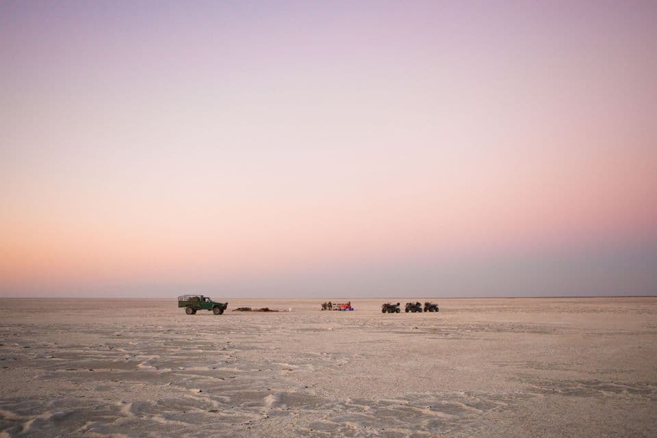 Un viaggio di gruppo WeRoad con un camion e dei quad è parcheggiato su una vasta distesa di sale asciutta al tramonto.