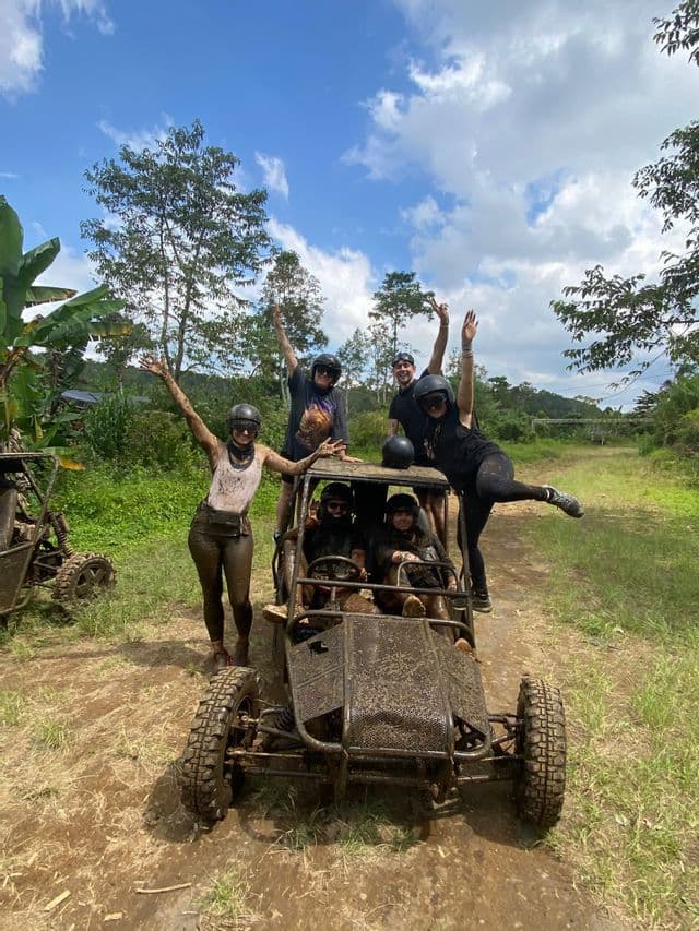 Un groupe WeRoad souriant, couvert de boue, pose avec son buggy tout-terrain sur un sentier de terre dans un cadre tropical.