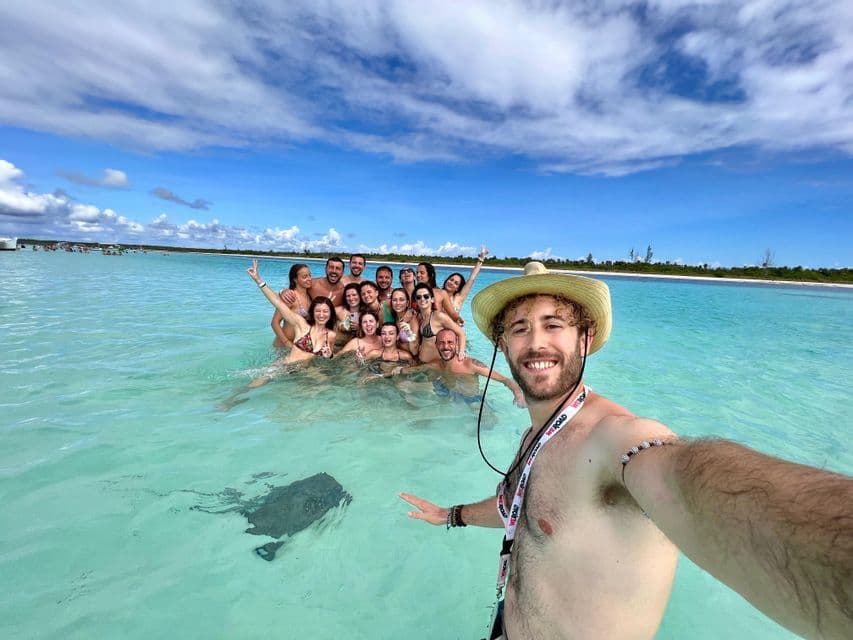 Un uomo con un cappello si fa un selfie con un viaggio di gruppo WeRoad e una razza nell'acqua bassa e turchese.