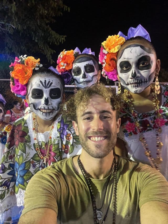 Un uomo in un viaggio di gruppo WeRoad si scatta un selfie con tre persone che indossano trucco da teschio e copricapi floreali per un festival notturno.