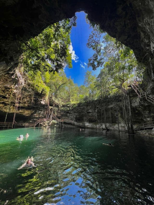 Un viaggio di gruppo WeRoad, nuotando nelle acque color smeraldo di un grande cenote, visto dall'interno della grotta.