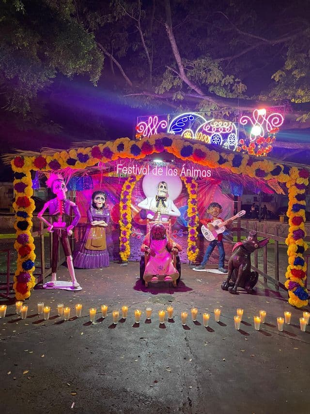 Un altare per il 'Festival de las Ánimas' decorato con calendule, luci al neon e grandi figure di scheletri, con candele accese davanti.