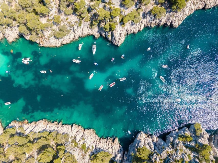 Una vista aérea de una cala rocosa llena de barcos y nadadores en agua turquesa vibrante.
