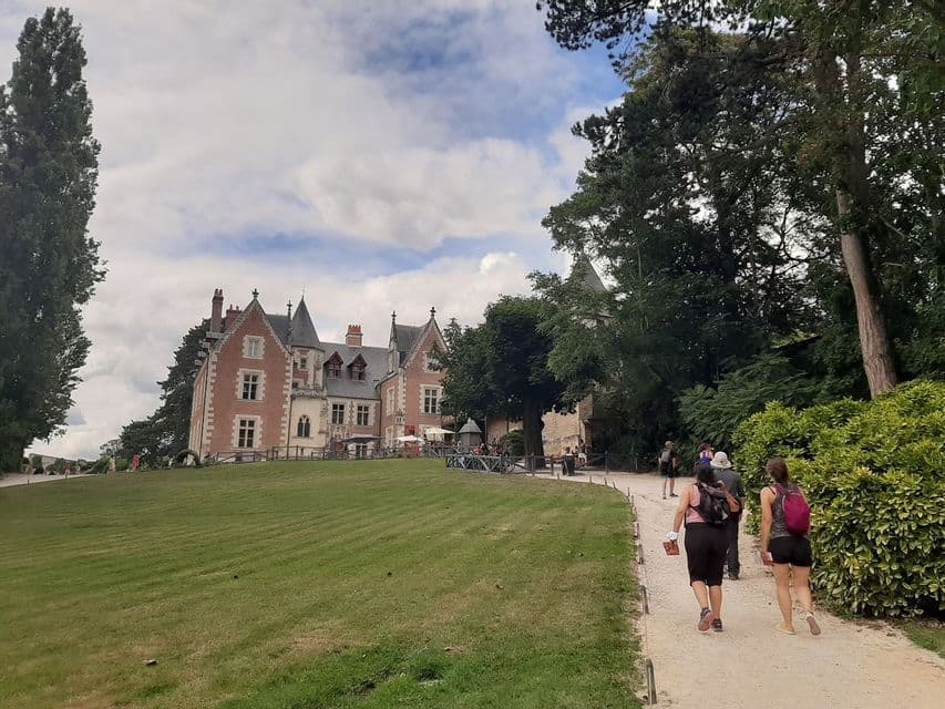 Un groupe WeRoad chemine le long d'un sentier vers un manoir historique en briques, avec une grande pelouse verte et des arbres.