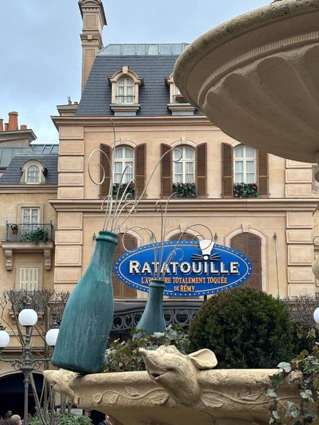 L'ingresso all'attrazione Ratatouille, con un'ampia insegna blu di fronte a un edificio in stile parigino e una fontana a tema.
