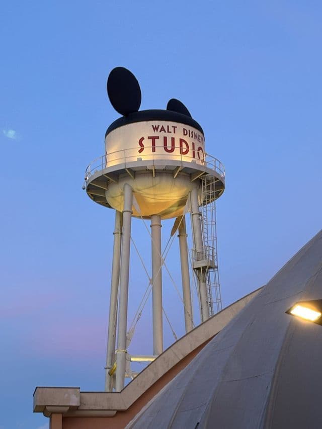 La torre dell'acqua dei Walt Disney Studios con grandi orecchie di Topolino in cima, illuminata contro un cielo crepuscolare.