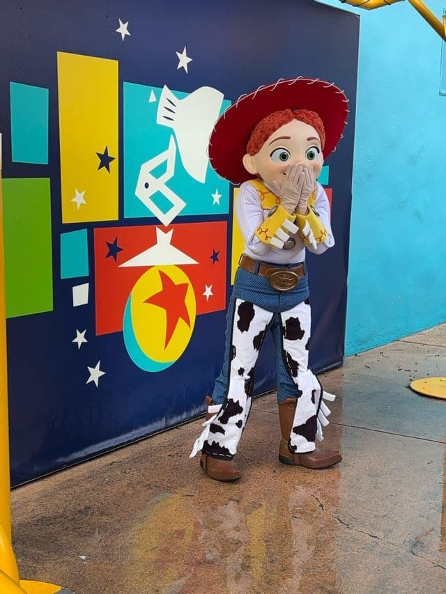 Jessie aus Toy Story im Kostüm posiert mit den Händen am Mund vor einer farbenfrohen Grafikwand.