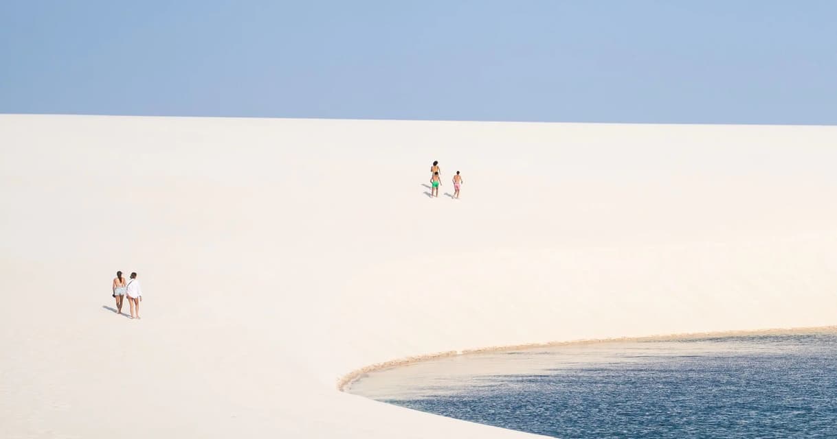 Un viaggio di gruppo WeRoad a piedi su vaste dune di sabbia bianca accanto a una laguna blu sotto un cielo limpido.