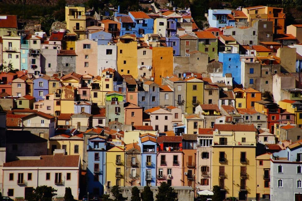 Un fitto insieme di case colorate con tetti rossi che ricopre una collina soleggiata.