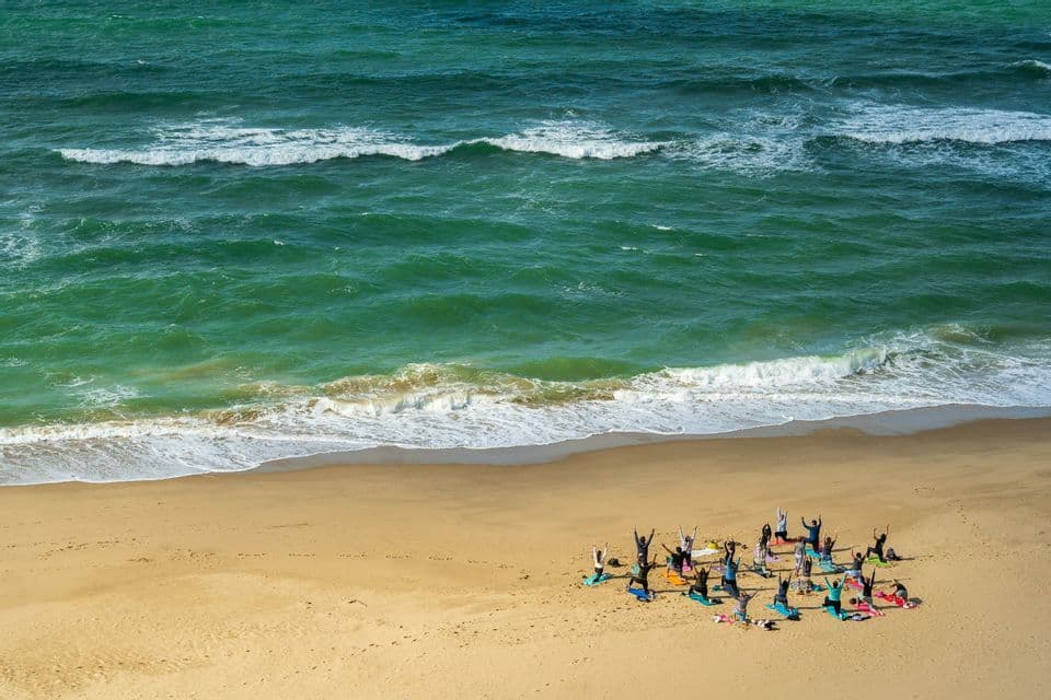 Un viaggio di gruppo WeRoad che pratica yoga su tappetini colorati su una spiaggia sabbiosa accanto all'oceano turchese.