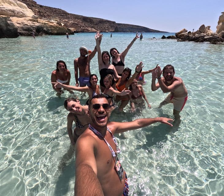 Un homme prend un selfie lors d'un voyage en groupe WeRoad dans l'eau claire et peu profonde d'une crique rocheuse.