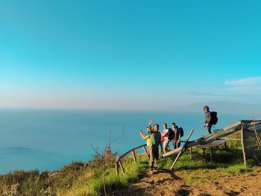 Eine WeRoad Gruppenreise mit Rucksacktouristen, die auf einem Küstenpfad mit Blick auf das blaue Meer unter klarem Himmel posieren.