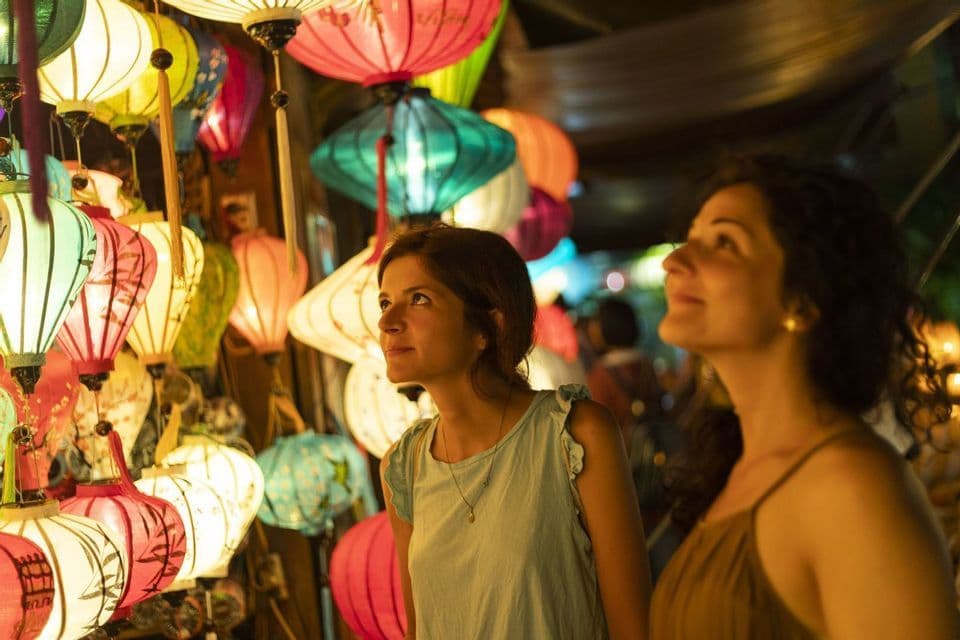 Dos mujeres observan un puesto de mercado nocturno, admirando una exhibición de coloridas linternas de papel iluminadas.