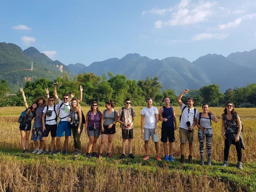 Un viaje en grupo de WeRoad posando para una foto en un campo dorado con un telón de fondo de montañas verdes bajo un cielo azul claro.