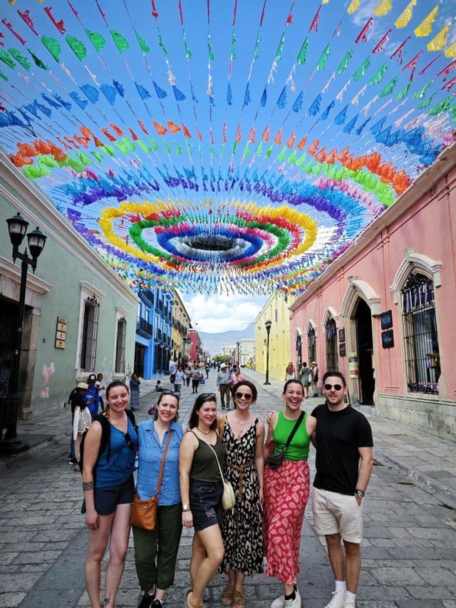 Eine WeRoad-Gruppe lächelt für ein Foto auf einer Kopfsteinpflasterstraße unter einem Baldachin aus bunten, festlichen Fahnen.