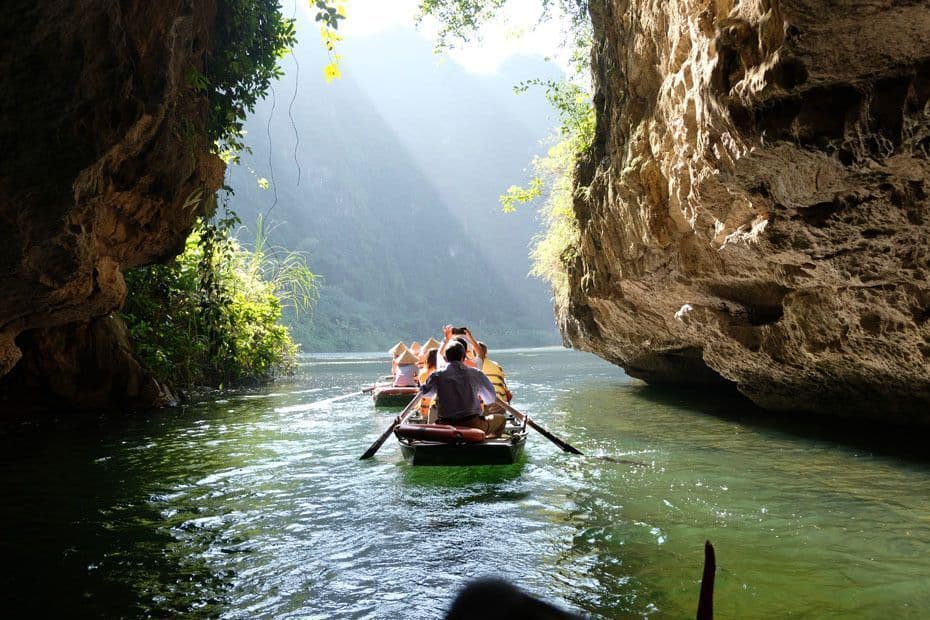 Un voyage en groupe WeRoad pagaie en petites embarcations sur une rivière ensoleillée, naviguant entre de grandes formations rocheuses luxuriantes.