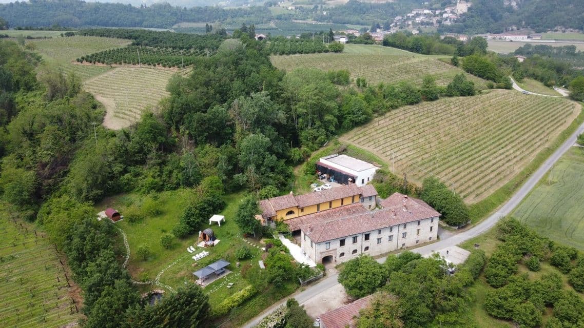Vista aerea di una tenuta di campagna con saune a botte, circondata da vigneti verdi e foreste su dolci colline